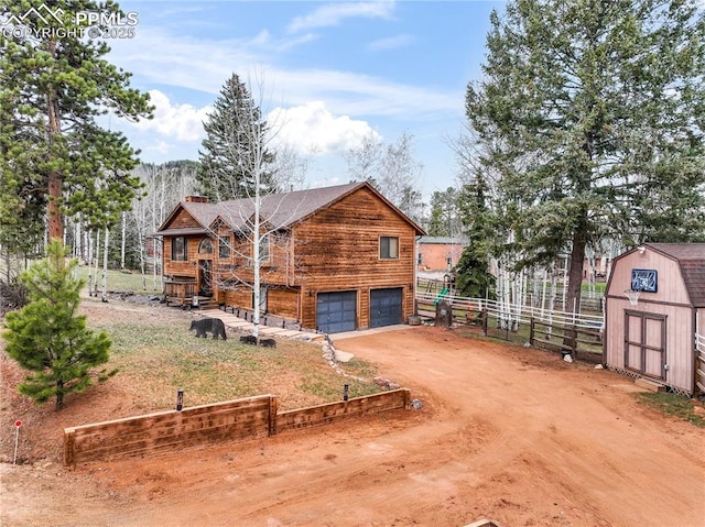 view of side of home featuring dirt driveway, a chimney, fence, a storage shed, and a garage