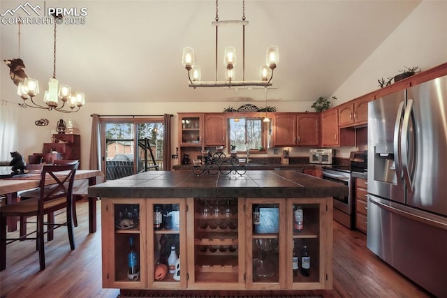 kitchen featuring brown cabinets, lofted ceiling, dark countertops, appliances with stainless steel finishes, and a notable chandelier