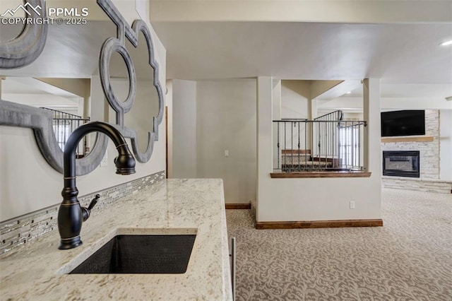 kitchen with baseboards, light stone counters, a fireplace, carpet flooring, and a sink