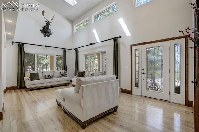 living room with a skylight, light wood-style floors, a towering ceiling, and baseboards