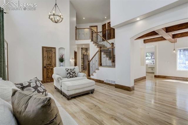 living room featuring visible vents, arched walkways, an inviting chandelier, light wood-style floors, and stairway