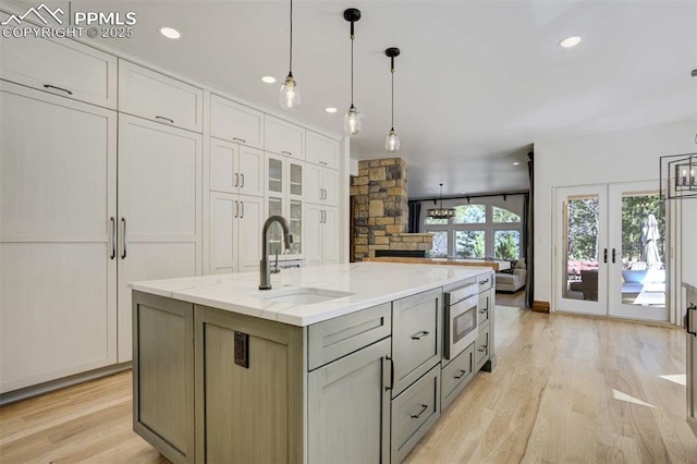 kitchen with white cabinets, a sink, stainless steel microwave, french doors, and light wood-style flooring