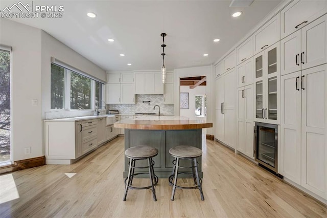 kitchen featuring wine cooler, a healthy amount of sunlight, a center island with sink, and light wood-style floors