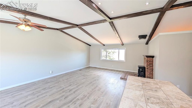 720 W Northwoods Dr, Woodland Park, CO 80863 - unfurnished living room with wood finished floors, a wood stove, baseboards, lofted ceiling with beams, and ceiling fan