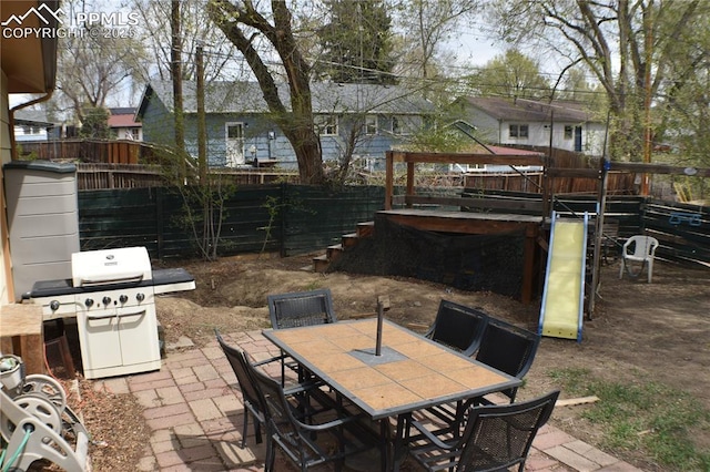 view of patio / terrace featuring a grill, fence, outdoor dining space, and a playground