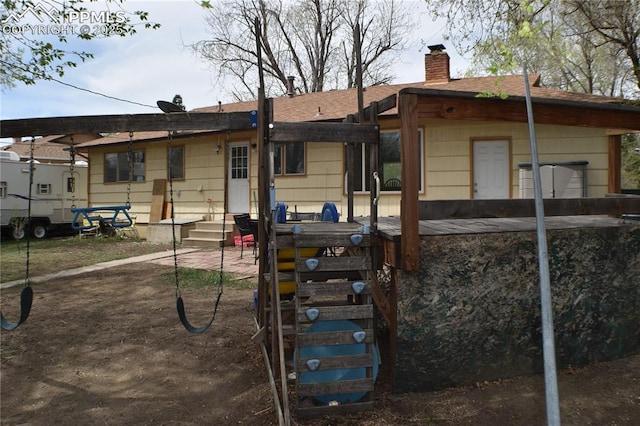 back of property with entry steps, roof with shingles, a patio, and a chimney