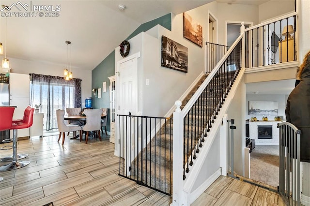 stairs featuring wood finish floors, baseboards, lofted ceiling, and a fireplace