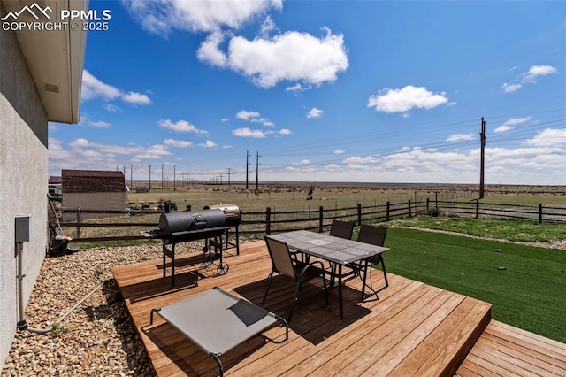 deck featuring fence, outdoor dining space, grilling area, a rural view, and a lawn
