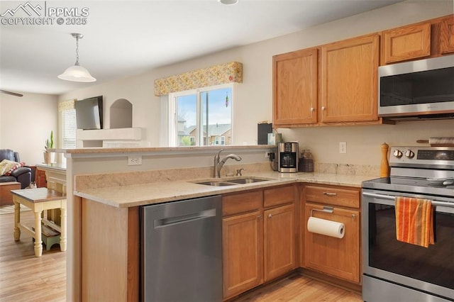 kitchen featuring a sink, light wood-style floors, stainless steel appliances, open floor plan, and a peninsula