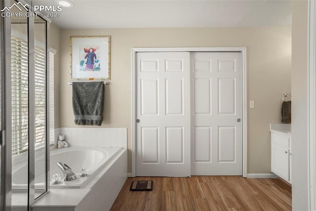 full bath with a healthy amount of sunlight, vanity, a garden tub, and wood finished floors