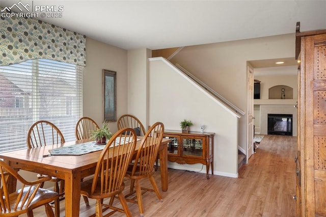 dining room with stairway, baseboards, a glass covered fireplace, and light wood-type flooring