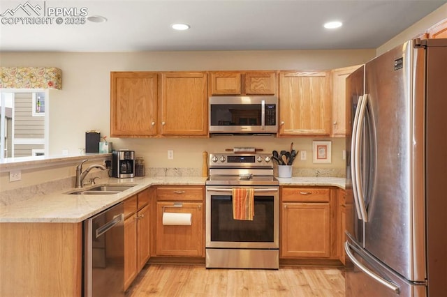 kitchen featuring appliances with stainless steel finishes, light stone countertops, a sink, a peninsula, and light wood-style floors