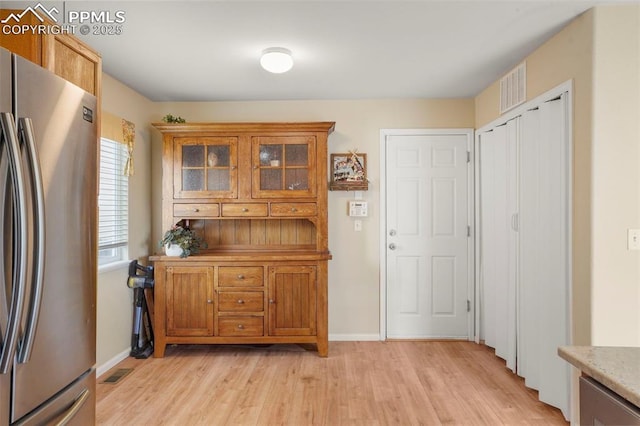 kitchen with freestanding refrigerator, baseboards, light wood-type flooring, visible vents, and glass insert cabinets