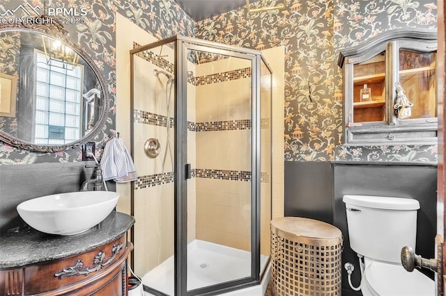bathroom with a shower stall, toilet, vanity, and wallpapered walls