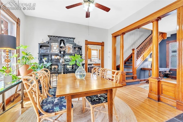 dining room with wood finished floors, a ceiling fan, stairs, and decorative columns