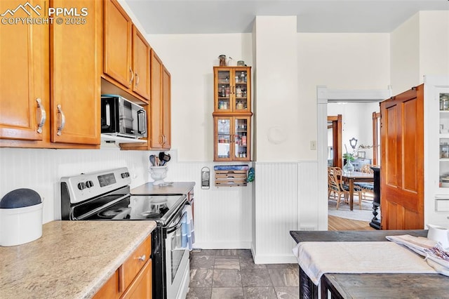 kitchen featuring brown cabinets, stainless steel range with electric cooktop, light countertops, black microwave, and wainscoting