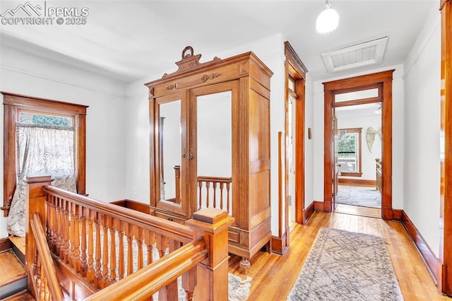 corridor featuring light wood finished floors, baseboards, visible vents, and an upstairs landing