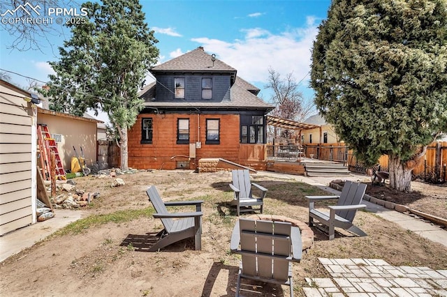 rear view of house featuring a fenced backyard, roof with shingles, a deck, and an outdoor fire pit