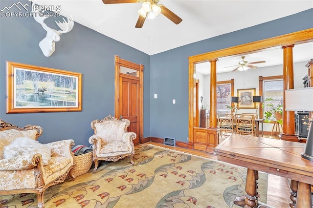 living area with baseboards, a ceiling fan, wood finished floors, and decorative columns
