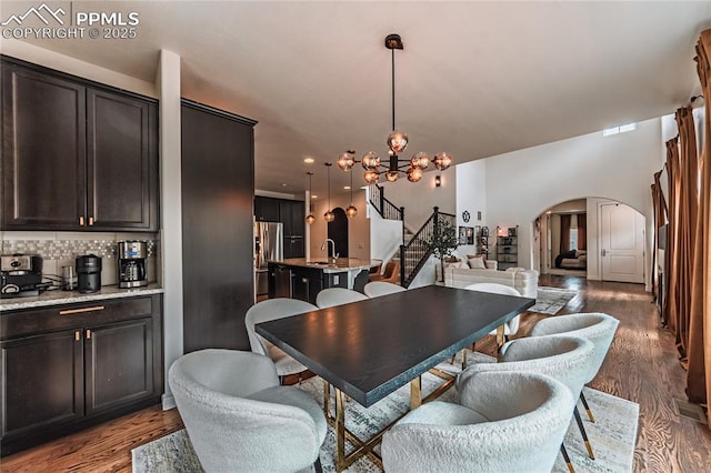 dining space with arched walkways, an inviting chandelier, stairs, and wood finished floors