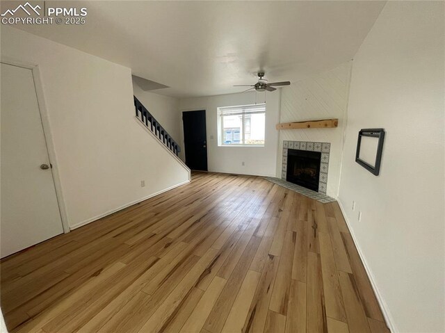 1426 Territory Trl, Colorado Springs, CO 80919 - unfurnished living room featuring baseboards, a tiled fireplace, ceiling fan, light wood-style floors, and stairway