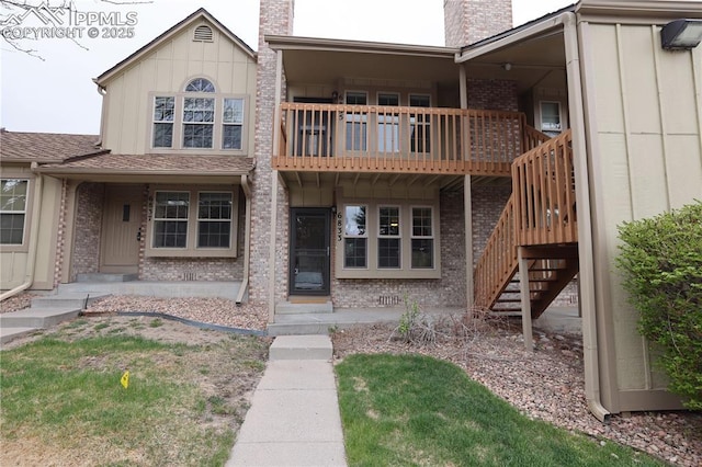exterior space featuring board and batten siding, a chimney, stairway, brick siding, and a balcony