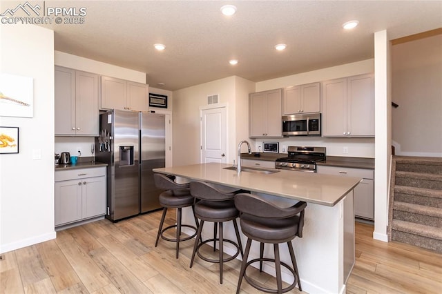 8162 Grey Bark Way, Colorado Springs, CO 80908 - kitchen with appliances with stainless steel finishes, a sink, gray cabinetry, light wood finished floors, and a kitchen breakfast bar