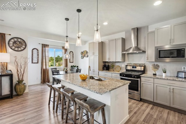 kitchen featuring wall chimney range hood, stainless steel appliances, a sink, and light wood finished floors