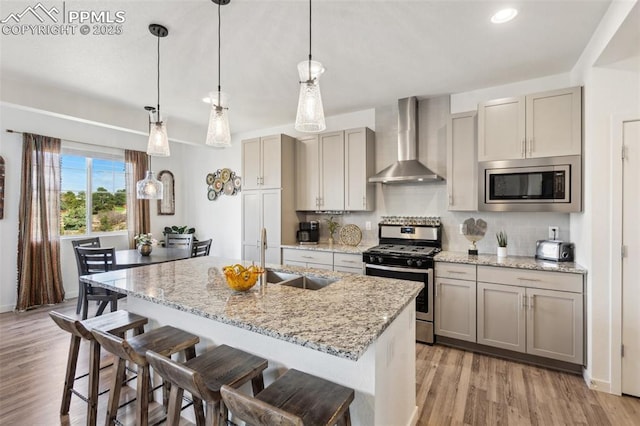 kitchen with wall chimney range hood, tasteful backsplash, a sink, light wood-style floors, and stainless steel appliances