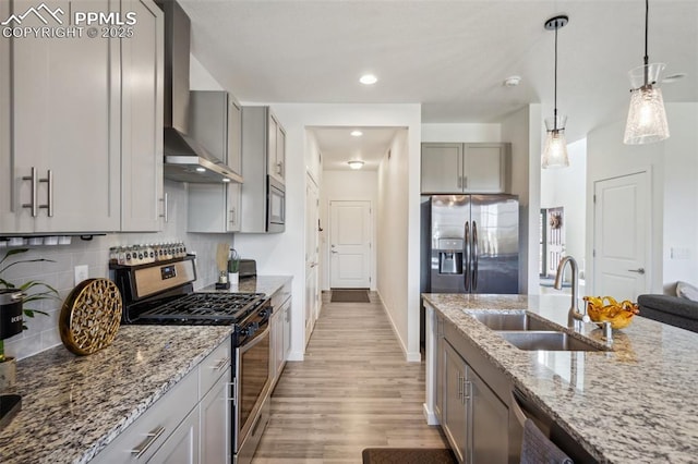 kitchen with wall chimney exhaust hood, light stone counters, a sink, light wood-style flooring, and appliances with stainless steel finishes