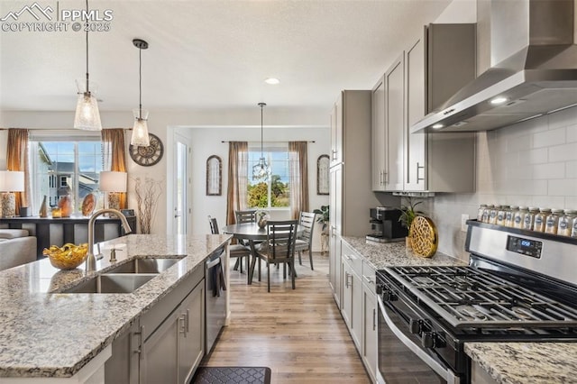 kitchen featuring decorative backsplash, light wood-type flooring, a sink, stainless steel appliances, and wall chimney exhaust hood