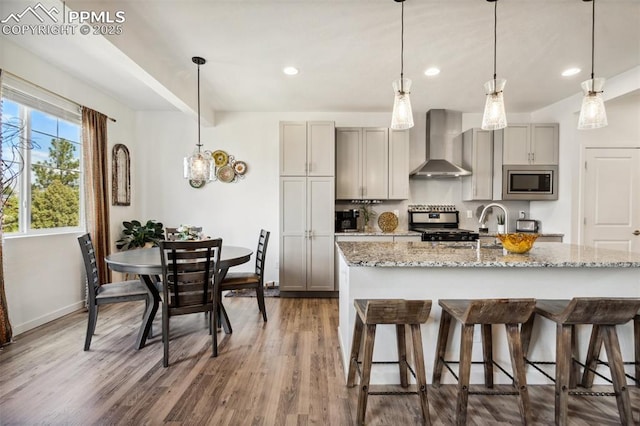 kitchen featuring baseboards, wall chimney range hood, a kitchen bar, appliances with stainless steel finishes, and gray cabinetry