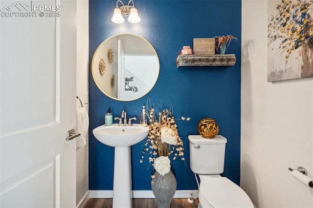 half bath featuring toilet, baseboards, a sink, and wood finished floors