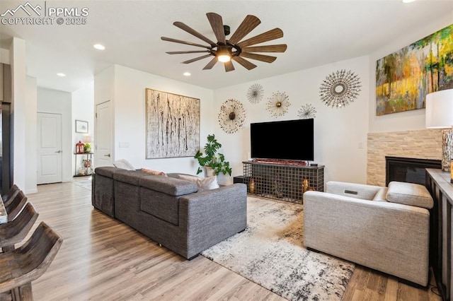 living room featuring a glass covered fireplace, a ceiling fan, recessed lighting, and wood finished floors