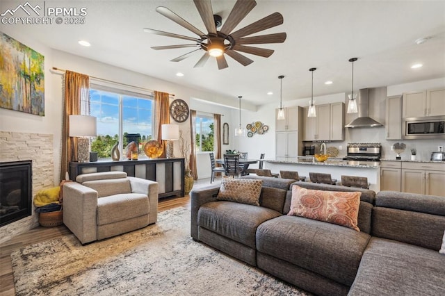 living area featuring recessed lighting, a ceiling fan, light wood-style flooring, and a stone fireplace
