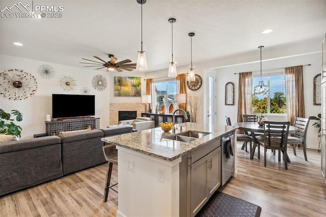 kitchen with stainless steel dishwasher, a sink, light wood finished floors, and ceiling fan with notable chandelier