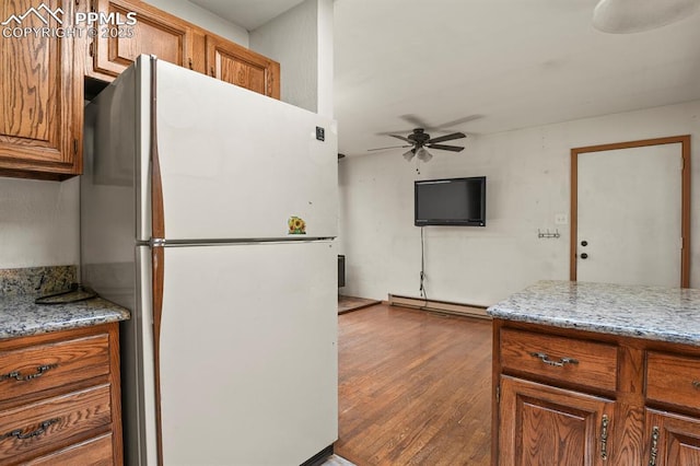 kitchen featuring freestanding refrigerator, brown cabinetry, ceiling fan, a baseboard radiator, and wood finished floors