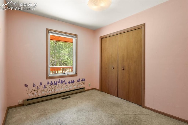 unfurnished bedroom with a closet, visible vents, carpet floors, baseboard heating, and baseboards