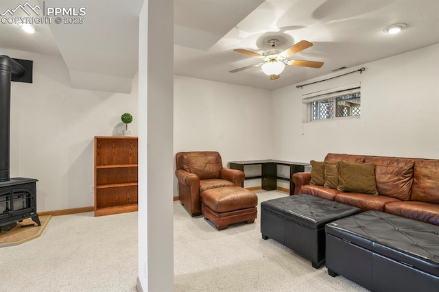 living room with visible vents, baseboards, a wood stove, ceiling fan, and light carpet