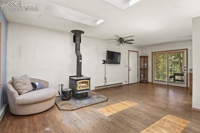 living area featuring ceiling fan, a wood stove, a skylight, wood finished floors, and a baseboard heating unit