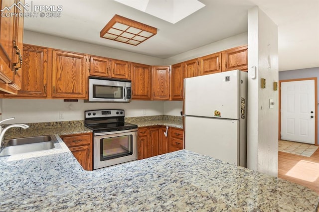 kitchen with brown cabinetry, a sink, light stone countertops, and stainless steel appliances