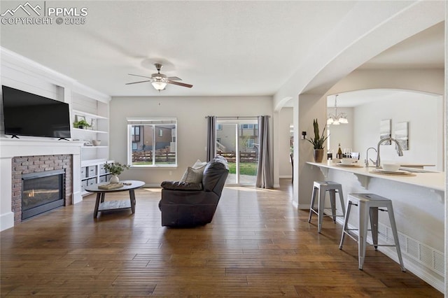 12529 Culebra Peak Dr, Peyton, CO 80831 - living area with dark wood finished floors, arched walkways, a brick fireplace, and ceiling fan with notable chandelier