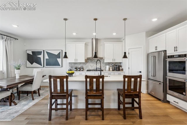 kitchen with tasteful backsplash, wall chimney range hood, light countertops, white cabinetry, and appliances with stainless steel finishes