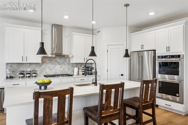 kitchen featuring wall chimney exhaust hood, light countertops, light wood-type flooring, stainless steel appliances, and backsplash