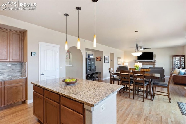 kitchen with arched walkways, tasteful backsplash, brown cabinets, open floor plan, and light wood-style flooring