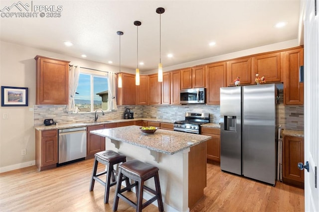 kitchen with brown cabinetry, a kitchen island, light wood-type flooring, a sink, and stainless steel appliances