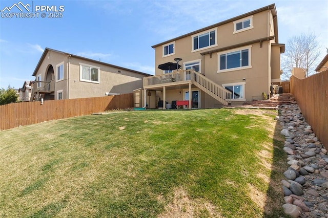 rear view of house with a lawn, a deck, a fenced backyard, stairs, and stucco siding