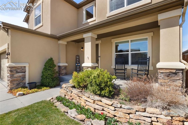 entrance to property with stucco siding, covered porch, and stone siding