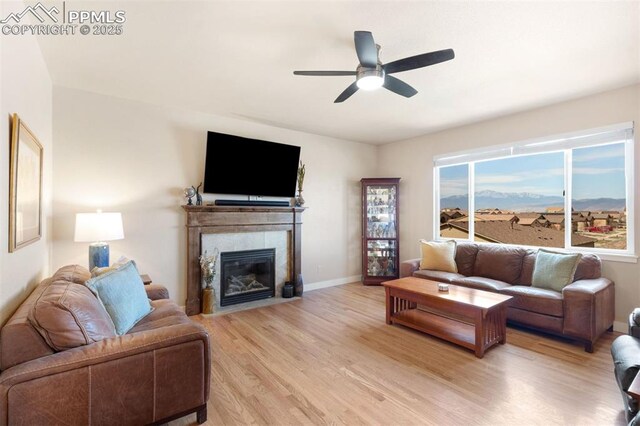 living room featuring a high end fireplace, a ceiling fan, light wood-style flooring, and baseboards
