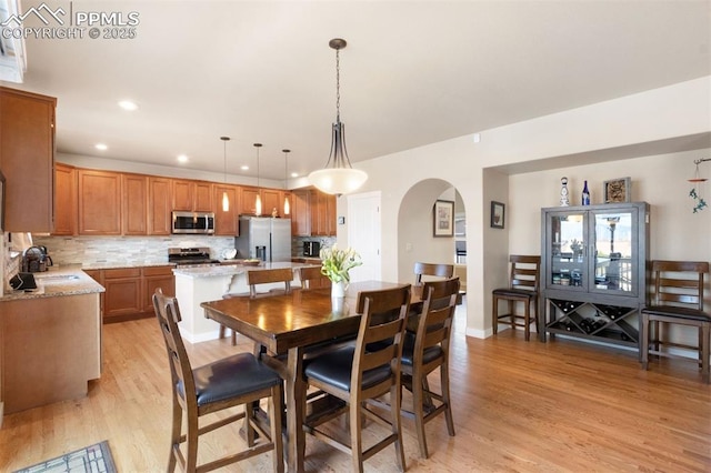 dining space featuring arched walkways, recessed lighting, and light wood-style flooring